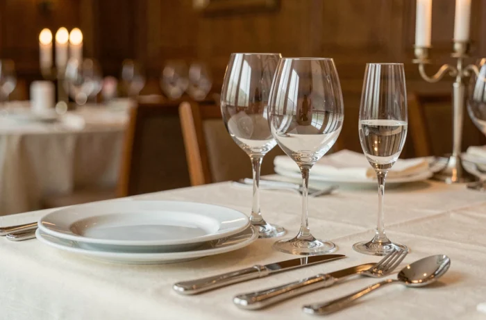 Disposition élégante de trois verres à vin en cristal sur une table de dîner gastronomique avec nappe ivoire et couverts en argent