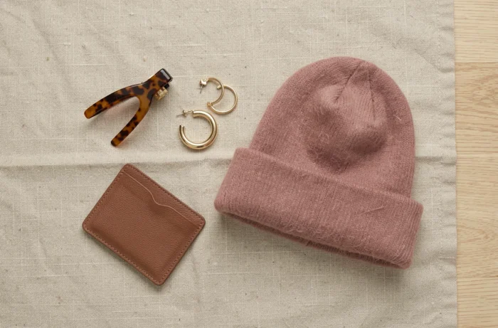 Flat lay d'accessoires de mode saisonniers sur fond de lin texturé, incluant bijoux, bonnet en cachemire et porte-cartes en cuir